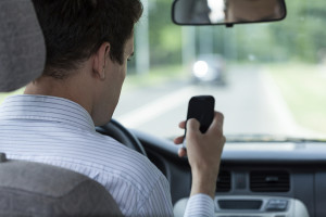A man uses his phone as he drives. He is a distracted driver.