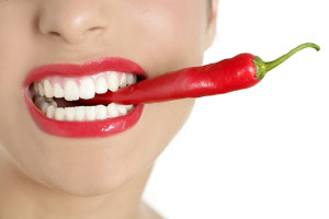 A woman eats a spicy red pepper.