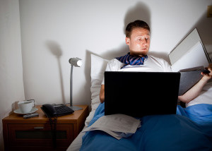 A man lies in bed, late at night, and works on his laptop.