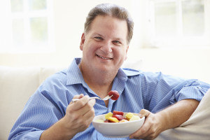 A man eats a bowl of fruit and smiles.