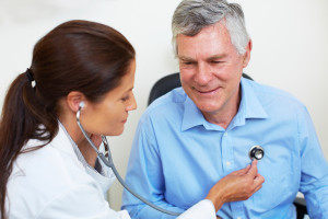 A medical professional uses a stethoscope to listen to an elderly man's heart.