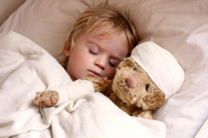 A child lies in bed with a stuffed animal and appears asleep.