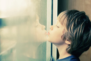 A young boy looks at his reflection in the window.
