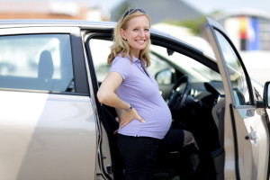 A pregnant woman smiles as she gets into the passenger seat of a car.