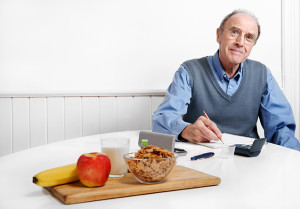 An elderly man appears to be journaling his food intake to improve his blood sugar levels.