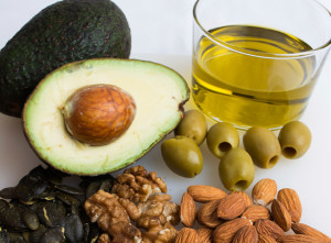 An avocado, olive oil, olives, almonds, walnuts and pumpkin seeds are shown.