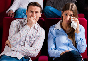 A woman and man tear up into a tissue at the movies.