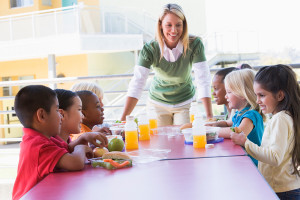 A group of preschoolers eat lunch together with an adult supervisor.