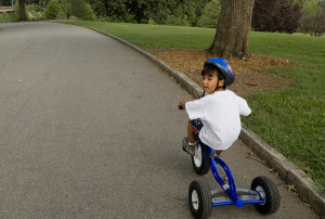 A young boy rides a blue tricycle. He wears a blue helmet.