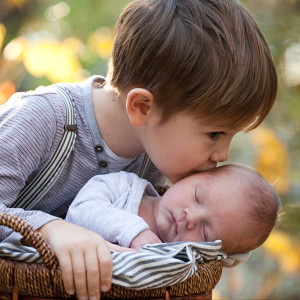 A young boy gives his infant broher a kiss on the forehead.