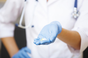 A medical professional's hand in a blue glove holds out white antibiotic pills.