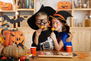 A young girl is dressed like a witch, and a young boy is dressed like a skeleton. They both wear face paint. 