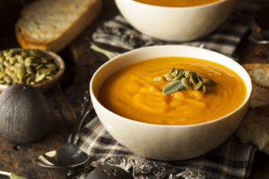 A squash soup is in focus with sunflower seeds on top.