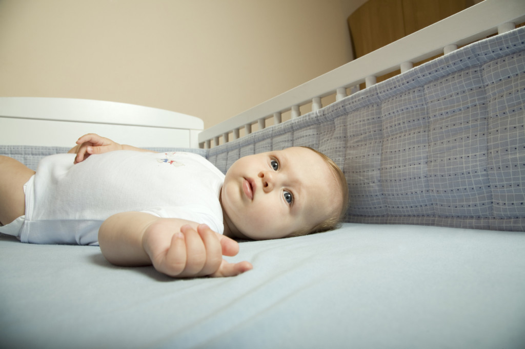 A young baby lies in a crib with crib bumpers.