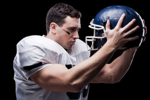A football player stares at the football helmet in his hands.