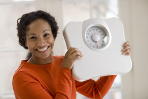 A woman holds a scale up in the air and smiles.