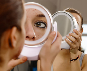 A woman looks at her acne in a mirror.