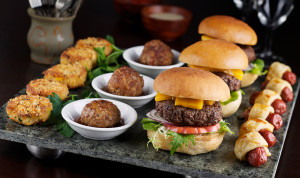 Cheeseburgers, pigs in a blanket, and more foods are served on a platter.