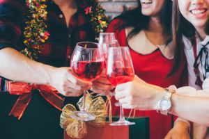Three people put their glasses of wine together for a toast. They appear to be celebrating a holiday.