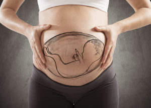 A pregnant woman shows off her pregnant belly. Her belly shows a drawing of a baby.