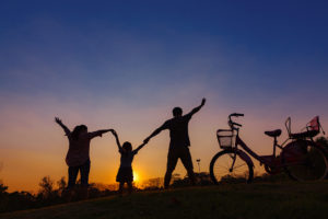 A family stands on top of a hill with their hands in the air as the sun rises.