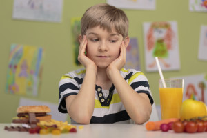 A young boy rests his head on his hands as he tries to choose between healthy and not-healthy options.