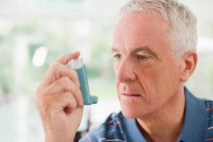 An elderly man holds his asthma inhaler and stares at it.