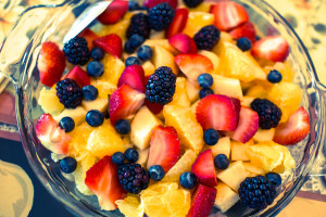 A large glass bowl holds strawberries, oranges, blackberries and blueberries.