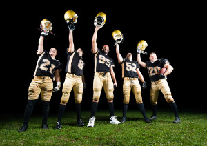 A group of football players hold their helmets up in the air and smile.
