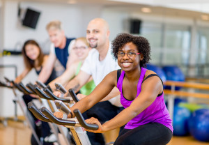 A group of people exercise on a stationary bike and smile.