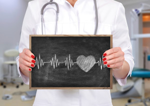 A medical professional holds a chalkboard. The chalkboard shows a drawing of a person's heart beat.
