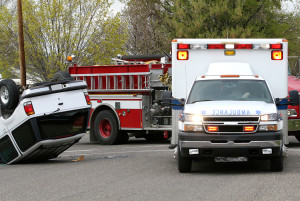 An ambulance and firetruck is shown next to an upside down car from a car crash.
