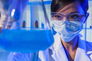 A medical professional is shown holding a beaker with a blue solution.