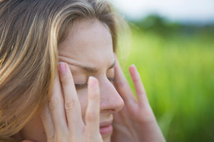 A woman holds her hands to her forehead and appears to be having a migraine.