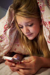 A young girl texts on her phone late at night.