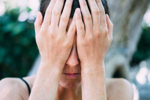 A woman covers her face with her hands and appears upset.