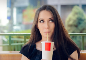 A woman drinks a large pop.