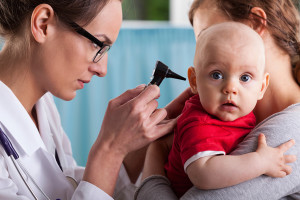 A medical professional looks at a baby's ear with an octoscope.