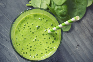 A green smoothie in a glass is shown with fresh spinach and a green- and white-striped straw.
