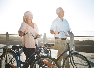 An elderly couple walks along a pier with their bikes.