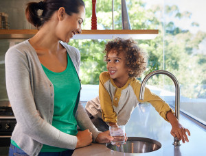 A mom fills a glass with water and hands it to her son.