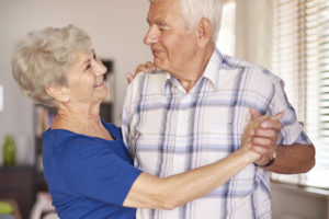 An elderly couple dances with each other and smiles.