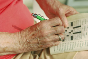 An elderly man fills out a crossword puzzle.