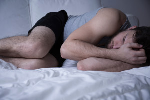 A man curls into a ball in bed and appears to be awake with insomnia.