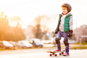 A young boy wears a helmet, knee pads and gloves as he skateboards outiside.