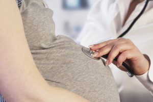 A medical professional places a stethoscope on a pregnant woman's belly to listen to the baby's heartbeat.