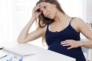 A pregnant woman leans her arm on a table and appears concerned.