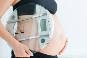 A pregnant woman holds a scale.