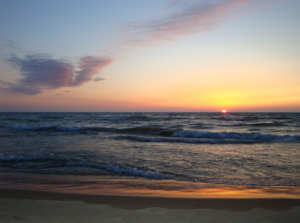 A view of the ocean is shown with the sun setting in the background.