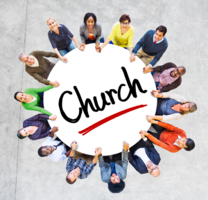 A group of people hold hands together. They sit at a table that says, "Church."